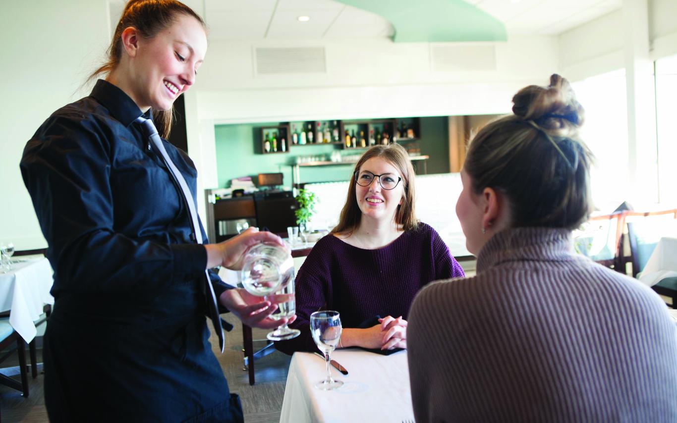 A Student of the Hospitality Management Diploma program serving two women