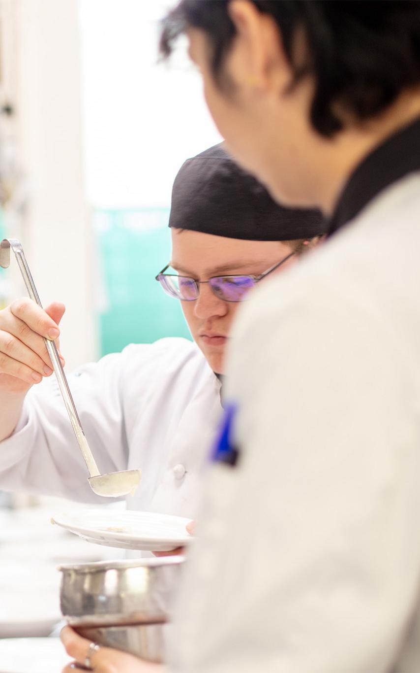 Culinary arts students in chefs whites preparing food. 