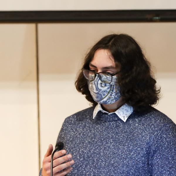A student wearing a blue sweater and facemask give their presentation.