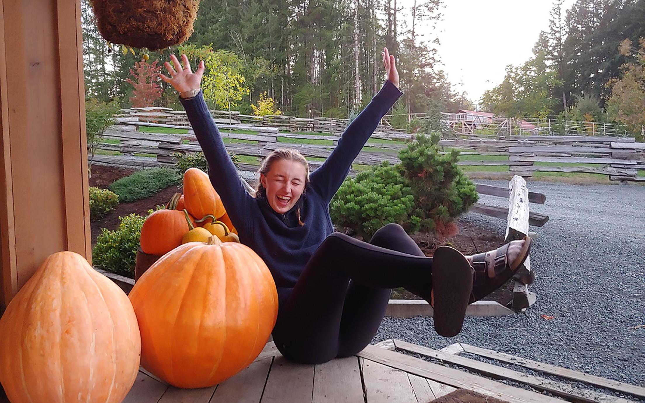 Girl poses with arms spread next to pumpkins