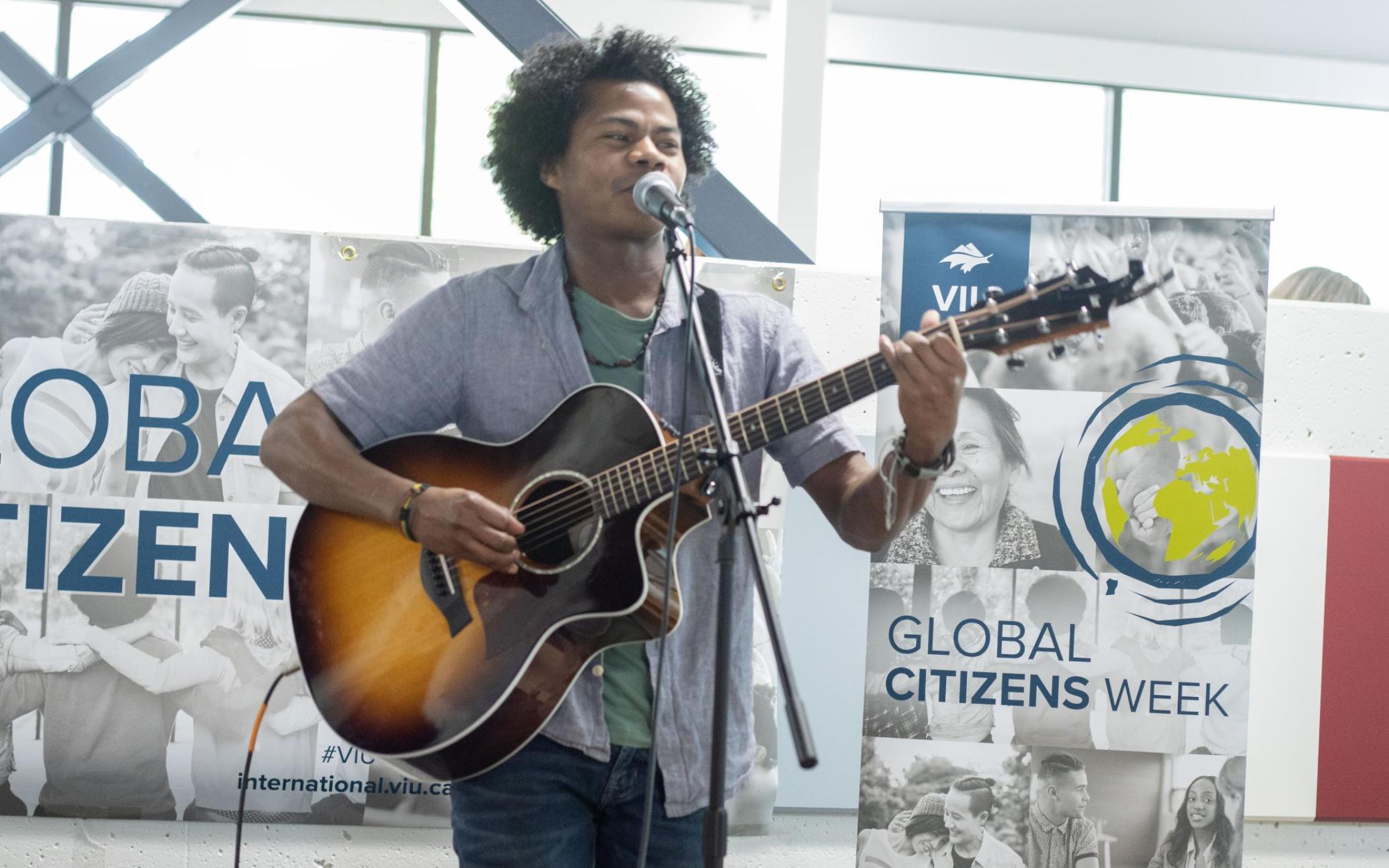 Student sings and plays guitar with Global Citizens Week banners behind him