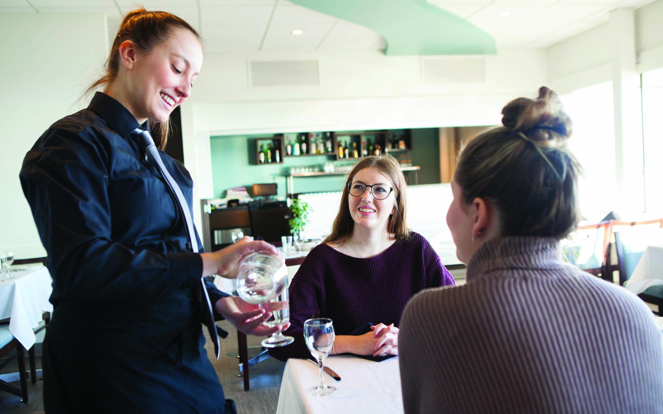 A Student of the Hospitality Management Diploma program serving two women