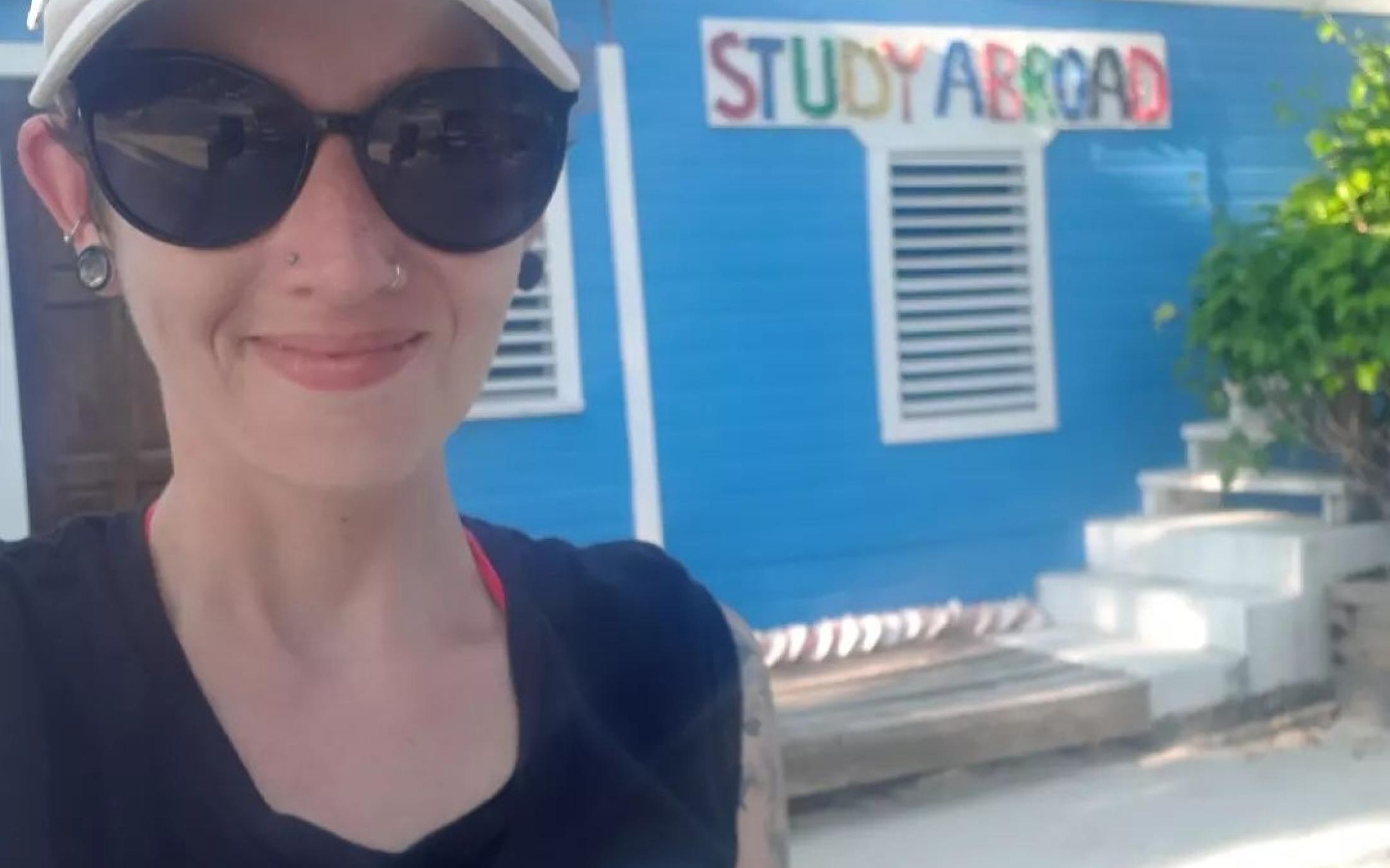 Melanie stands in front of the Tobacco Caye sign, which reads Study Abroad underneath it