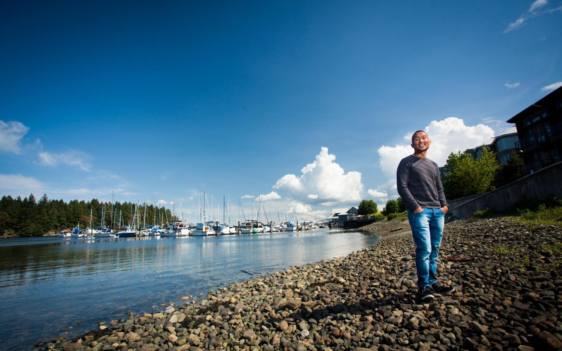 A man stands in the foreground with the waterfront and a marina full of boats behind him
