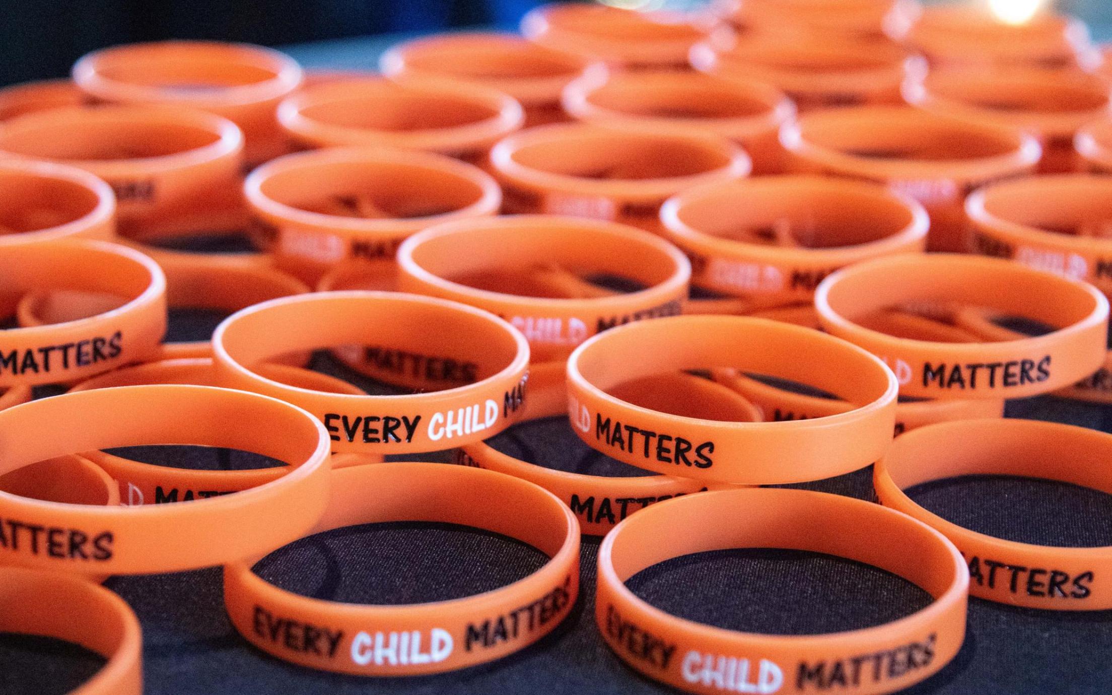 Dozens of orange bracelets that read Every Child Matters
