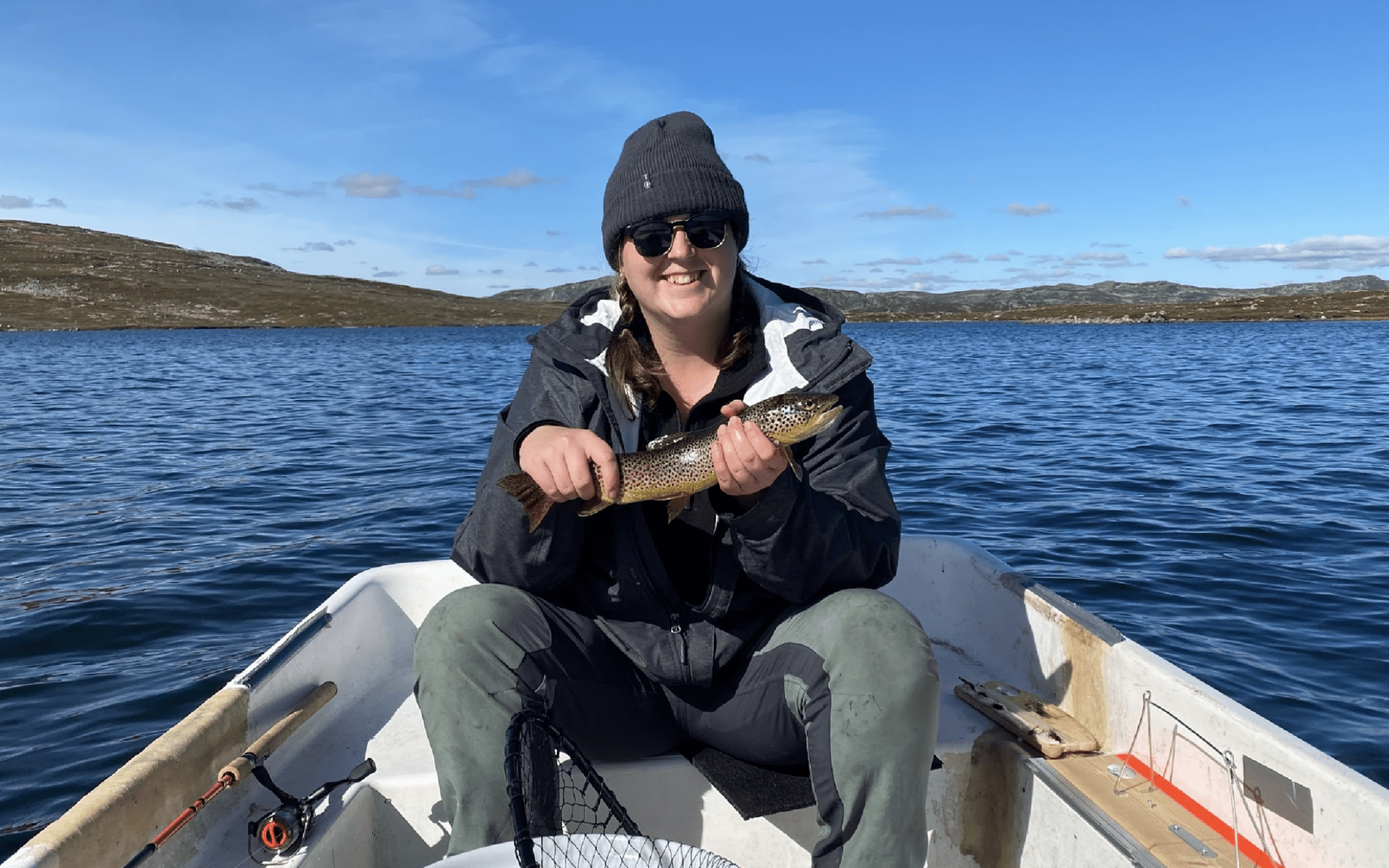 Sarah Osborne sitting in a boat holding a fish and smiling at the camera