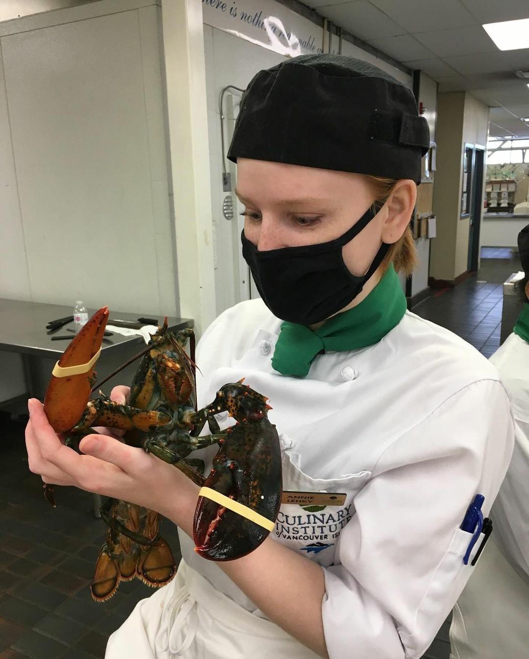Girl wearing VIU Culinary Arts uniform holding a lobster