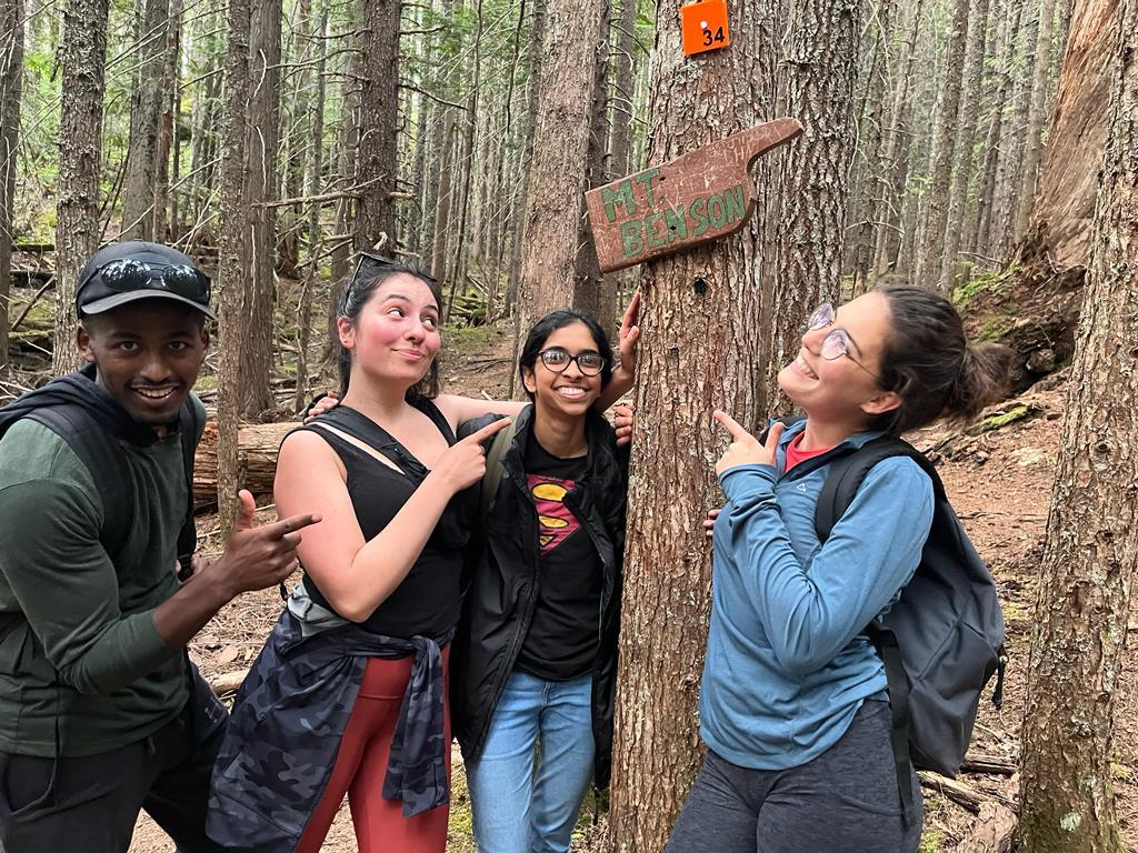 Four people stand next to a sign on a tree that points up