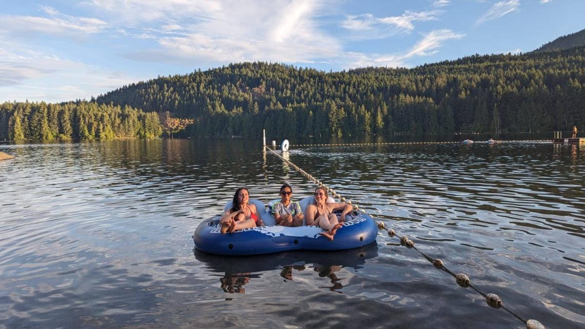 three people lounge in an inner tube in a lake