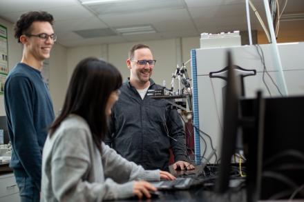 three people stand around a mass spectrometer