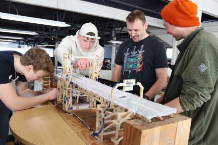 Four students bend over a bridge structure together