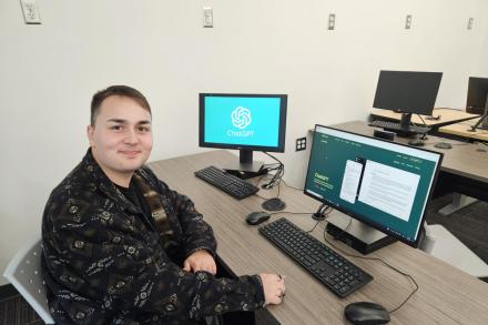 Andrew Szilagyi sitting in front of a computer and smiling at the camera. ChatGPT is on the screen in the background.