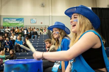 Women wearing blue bang on drums