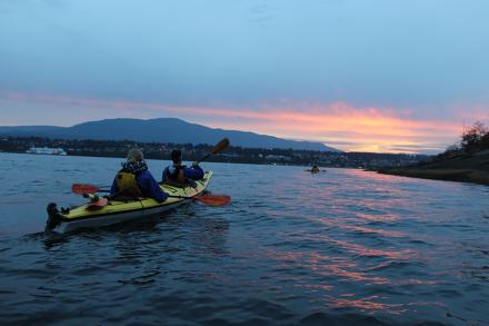 Two people kayaking towards a sunset.