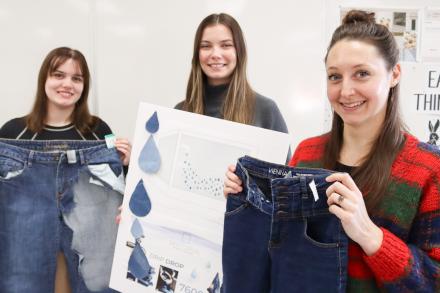 Two students hold up jeans and another holds up a poster.