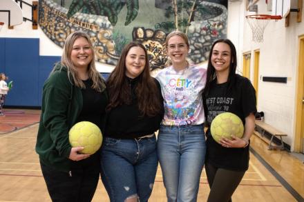 Four students in a gym holding volleyballs