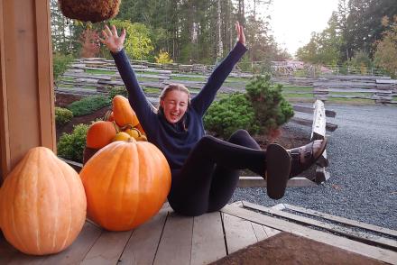 Girl poses with arms spread next to pumpkins
