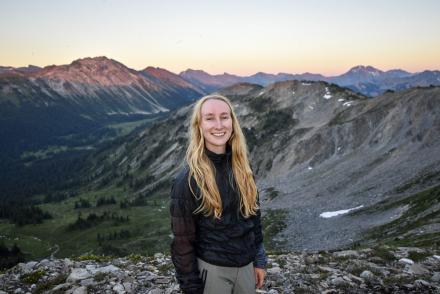Kelsey Moore smiles with a mountain range at sunset behind her.