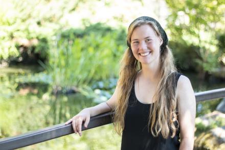 Michaela Medina stands in front of the VIU koi pond, smiling.
