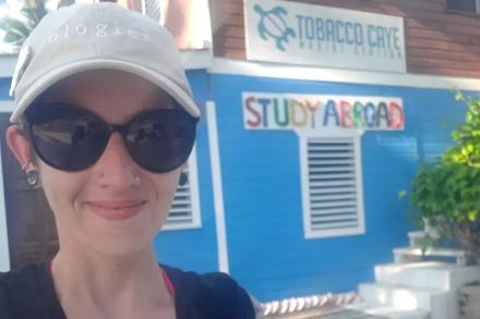 Melanie stands in front of the Tobacco Caye sign, which reads Study Abroad underneath it