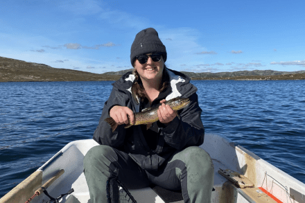 Sarah Osborne sitting in a boat holding a fish and smiling at the camera