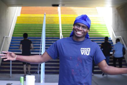 Black student holds arms out in welcome standing in front of the rainbow stairs