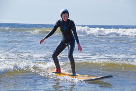 A woman wearing a wetsuit stands up on a surfboard