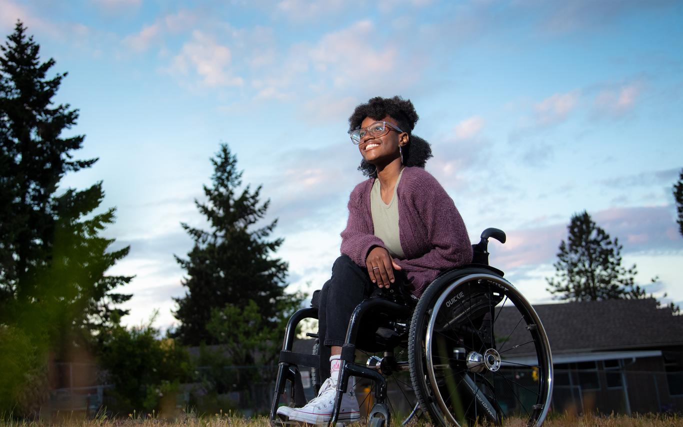 Woman in a wheelchair outside among a stand of trees. 