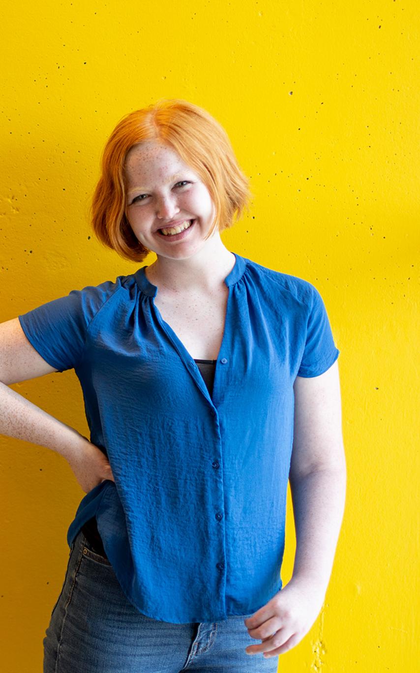 Smiling young woman standing in front of a yellow wall.